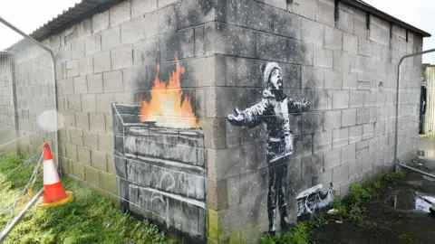 PA Media A Banksy piece of art on the side of a garage near the steelworks depicting ash from a fire falling on a child like snow.