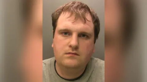 Cumbria Police Police custody image of Jonsen Lamb. He has brown hair and is wearing a grey jumper. He is looking into the camera.