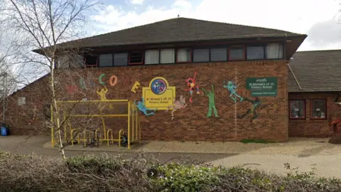 Google The outside of the school building near it's entrance with a few trees and bushes and a yellow bike locking shelter outside