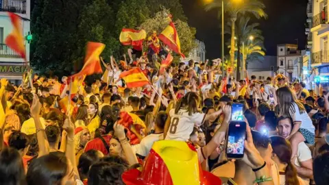 Dozens wave Spanish flags and celebrate Spain's win in a square in Seville 