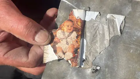 Supplied Close-up of Alan Needham's hands holding a slate with a torn photograph of a baby attached to the surface.