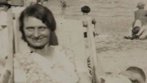 Supplied Black and white photo of Louisa Dunne. She is sat on a deck chair looking at the camera and smiling. 