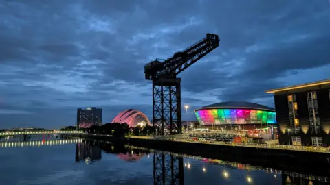 Deborah Currie Brightly lit colourful buildings set against a dark sky and River Clyde.