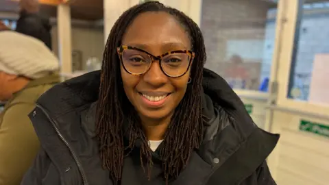 A picture of Natalie Nelson at the family tree class, smiling into camera. She has long black braids and is wearing a thick black coat