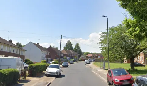 Google Maps Mickleham Road with houses on the left with cars parked on the pavements lining some of the street and grass on the opposite side to the right with a bus stop in the distance.