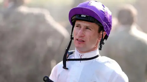 Getty Images Oisin Murphy, a man wearing a white shirt and a purple helmet, looking at something off camera.