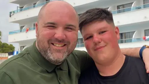 Morgan and his father arms around each other smiling at the camera