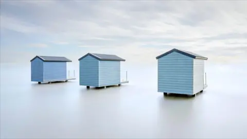 John Law Three blue beach huts are standing in what appears to be an empty plain.