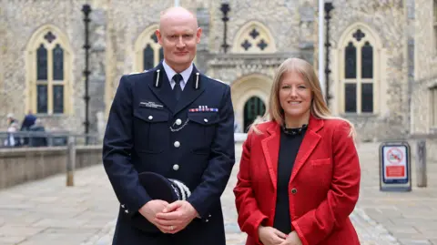 Alexis Boon, standing in police uniform and holding a police hat, stood next to Donna Jones, who is wearing a red jacket and a black top underneath it.