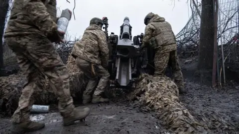 Soldados ucranianos da EPA se preparando para atirar no Hovitzer na área de Kharkiv - os três homens carregaram a arma, 18 de janeiro.