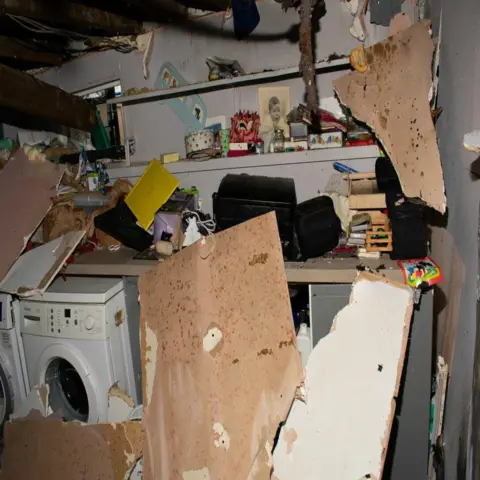 PA Wooden parts of the roof are scattered around the room in pieces against a shelf of trinkets and photos. 