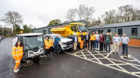 Wokingham Borough Council Wokingham Borough Council staff and offices posing in front of their new offices with a gritter, a response vehicle and a road sweeper.