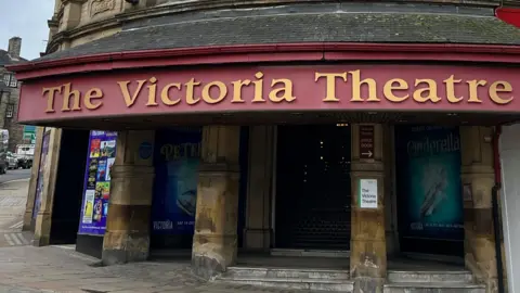The outside of the Victoria Theatre in Halifax - a grand stone building with red and gold signage above the front