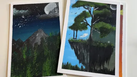 Two paintings on a white table. On the left, there is a grey mountain speckled with white snow. It is surrounded by tall green trees. There is a dark blue starry sky with a white moon and grey fluffy clouds. The other, on the right, is a floating island with a large tree on it. Half of the tree is in the daylight with a blue sky, clouds and birds. The other side is at night time, with a dark sky and stars