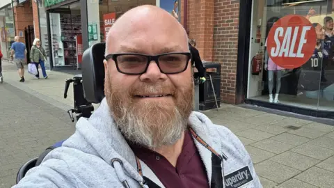 Supplied Man with beard in grey hoodie in wheelchair on high street