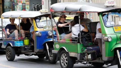 Tourists travel on tuk-tuk taxis in Bangkok.