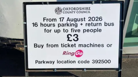 A white sign with black writing. It reads "from 17 August 2026 16 hours parking and return bus for up to five people £3".