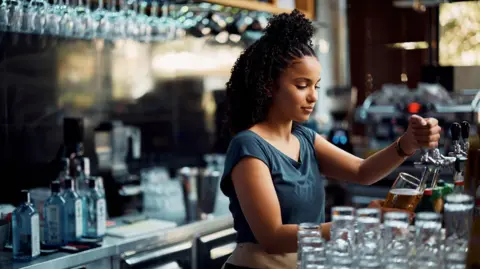 Getty Images Young waitress pouring draft beer while working at bar counter. 