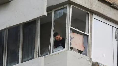 Reuters A man inspects damage inside an apartment which had its windows blown out in a drone attack on Tel Aviv (19/07/24)