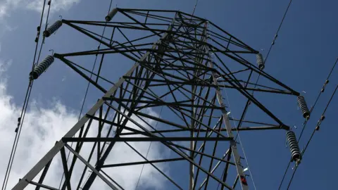 Looking up from the ground to a giant dual-line electricity pylon against a blue sky