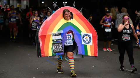 Getty Images A lady smiling on the track, dressed as a rainbow wearing an official World Record attempt sticker and poster saying 'empowering blind children and young adults'.