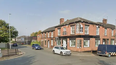 A traffic lights junction on Oldham Road, Middleton, Rochdale, Greater Manchester, on a sunny day.