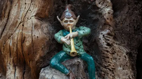 A wooden carving of an elf plays a musical instrument in a tree