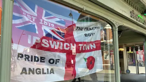 Ben Parker/BBC A pub window with a flag that reads Ipswich Town, Pride of Anglia and The Tractor Boys.