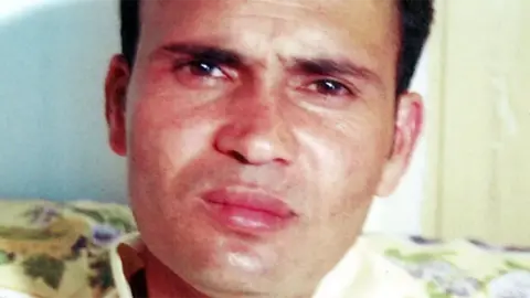 A man with short, brushed black hair sitting on a floral sofa and looking at the camera