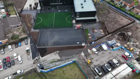 An aerial picture of a large building with a football pitch and fenced off area with two car parks either side of it