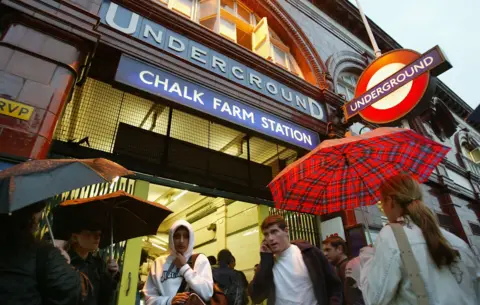 Getty Images People, some using umbrellas wait outside of a closed Chalk Farm Underground station 