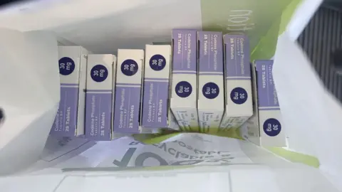 Evie Solomon A picture of purple and white tablet boxes in a paper bag from a pharmacy.