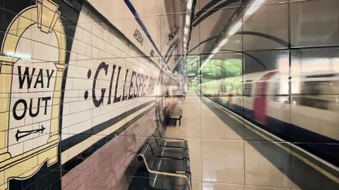 A picture of a London Underground station, printed on a tiled display. The words way out can be seen on an ornate sign to the left of the image