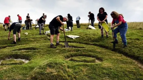 National Trust Group of people with spades digging the edges of large chalk figure, the Cerne Giant.