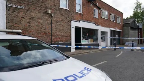 PA Media A police car is parked across the crime scene in Fountain Lane in Boston. Blue police tape block the road outside the shop