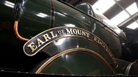 A green steam locomotive in a railway shed. In golden lettering are the words Earl of Mount Edgcumbe
