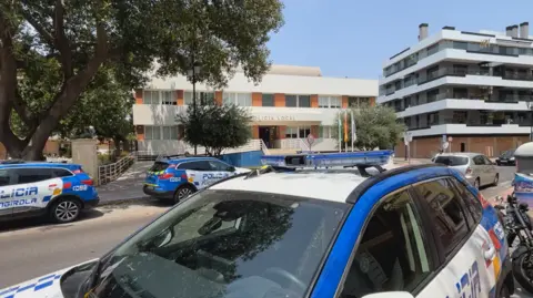 A Spanish police station with at least three blue and white police vehicles parked in the street outside.
