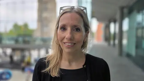 Paul Moseley/BBC Sarah Taylor is wearing a black top and smiling. Her glasses are placed on top of her head.