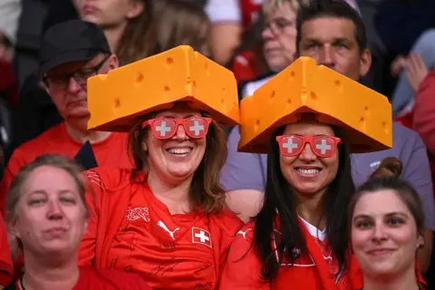 Getty Images Two Swiss fans wear sunglasses in the colours of Switzerland's flag and hats that resemble wedges of Gruyère cheese