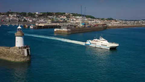 A passenger ferry leaving St Peter Port Harbour. You can see St Peter Port sea front in the background.