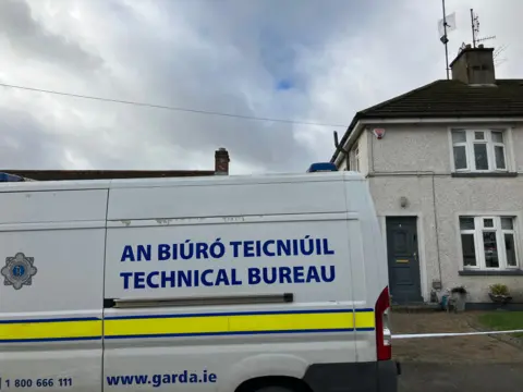 A white house, taped off with police tape
There is a white Garda van that reads technical bureau parked outside