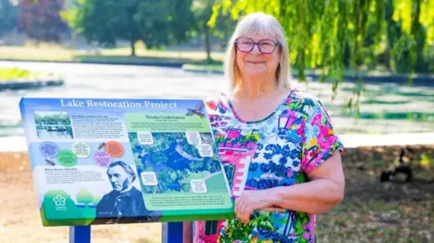 Leicester City Council Woman smiling next to information panel with lake in the background