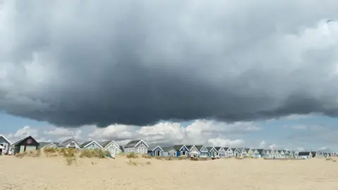 BBC Weather Watcher, LouieMurg Mudeford, Dorset - beach with a row of huts behind and low grey clouds above.