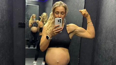 Family handout Becki Barratt, who is wearing a sports bra so her baby bump is on display, is posing for a selfie in front of a mirror. She has flexed her left arm and holds the camera phone in the other. 