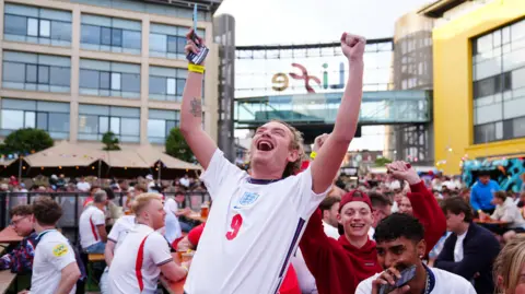 Owen Humphreys/PA A man standing from his table and cheering with his fist in the air. In his other hand there is a phone, so he may have actually been taking a video or call. Who can say for sure?