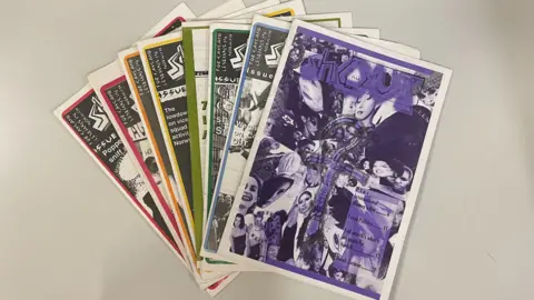 Emma Craig/BBC A pile of magazines and newspapers spread out on a table. They each have different artwork on the front and within the pile there is a red, pink, orange, yellow, green, blue and purple items.