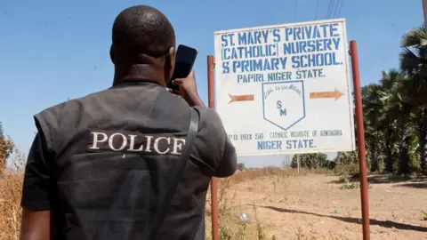 EPA A member of the security forces, with his back to the camera and his jacket written Police takes photos of St Mary's Private Catholic School signage in Papiri
