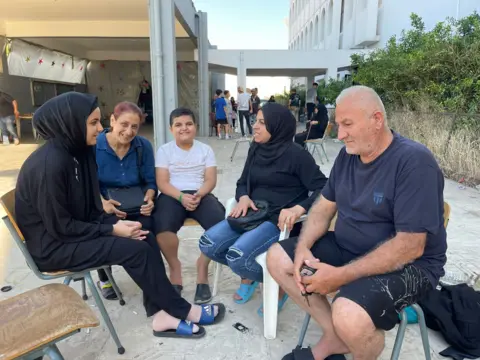 Kamal Mouhsen and his family sit on classroom chairs in the courtyard of the school that is now their home