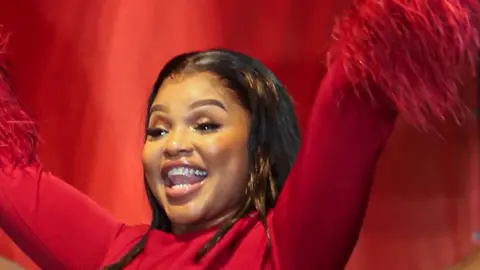 A woman dressed in red stands on stand with her arms in the air.