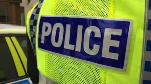 Close-up picture of a police jacket, featuring a blue section bearing the words 'police' on top of a yellow high-vis section.